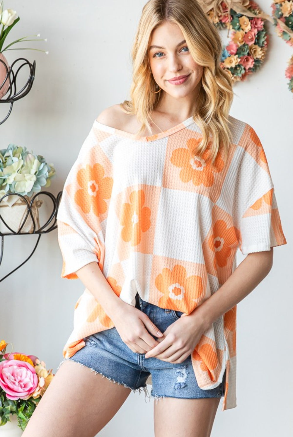 Woman wearing an orange V-neck floral checkered T-shirt, paired with denim shorts for a chic summer look.
