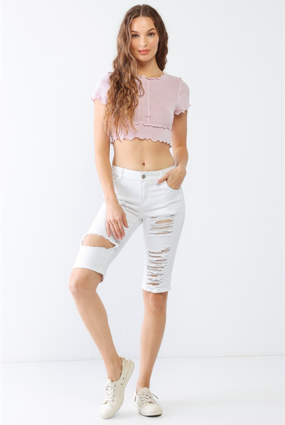 A model wearing white distressed bermuda denim shorts, styled for a chic and casual summer look.