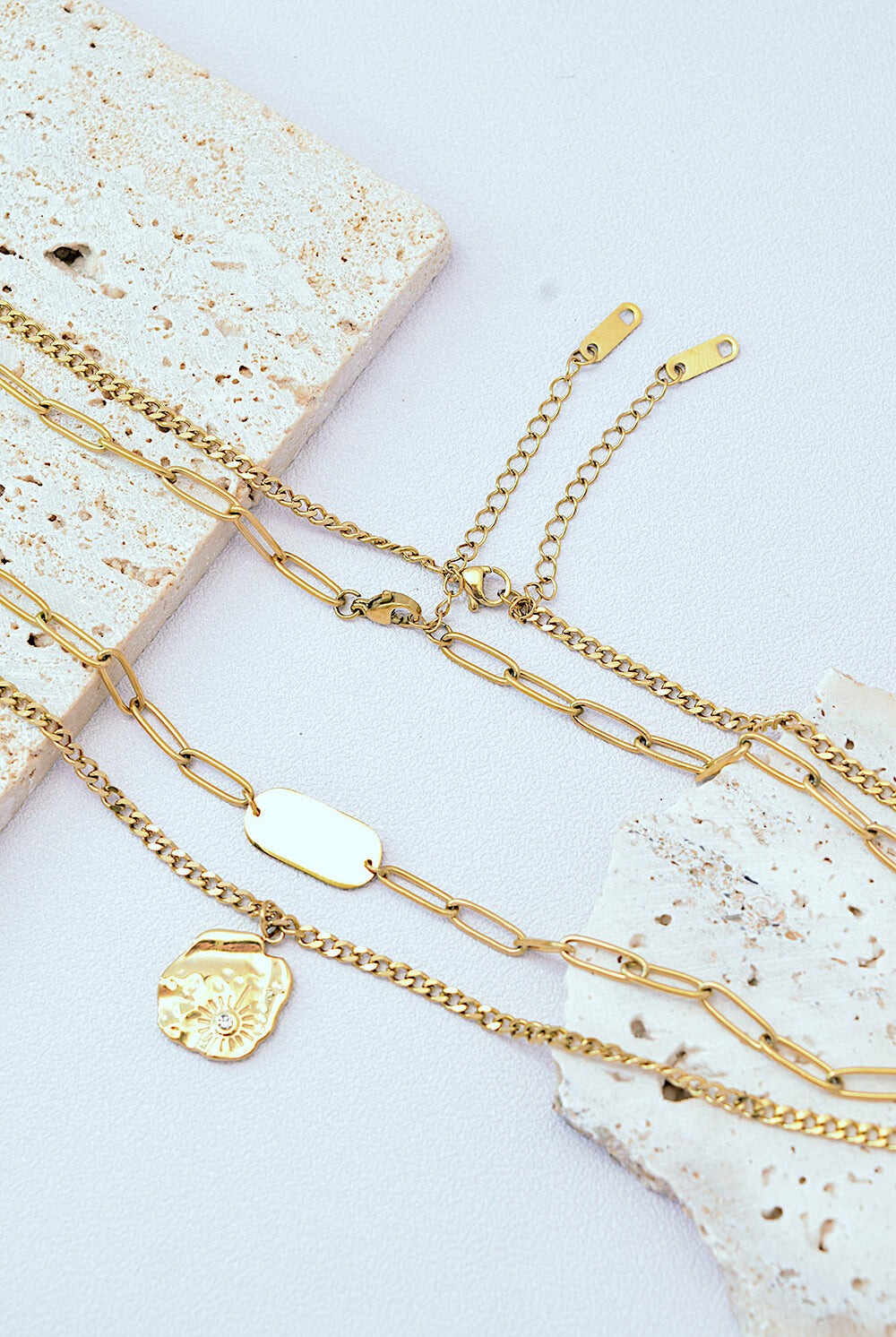 Gold-plated double-layered necklace featuring a bar detail on the upper chain and a detailed circular pendant on the lower chain, set against a white background.