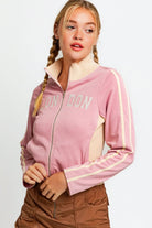 Trendy young woman showcasing a soft pink zip-up jacket with "LONDON" embroidered across the chest.