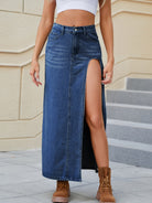 Woman in a light-wash high-waisted denim maxi skirt with a thigh-high slit, paired with a white crop top and brown lace-up boots.