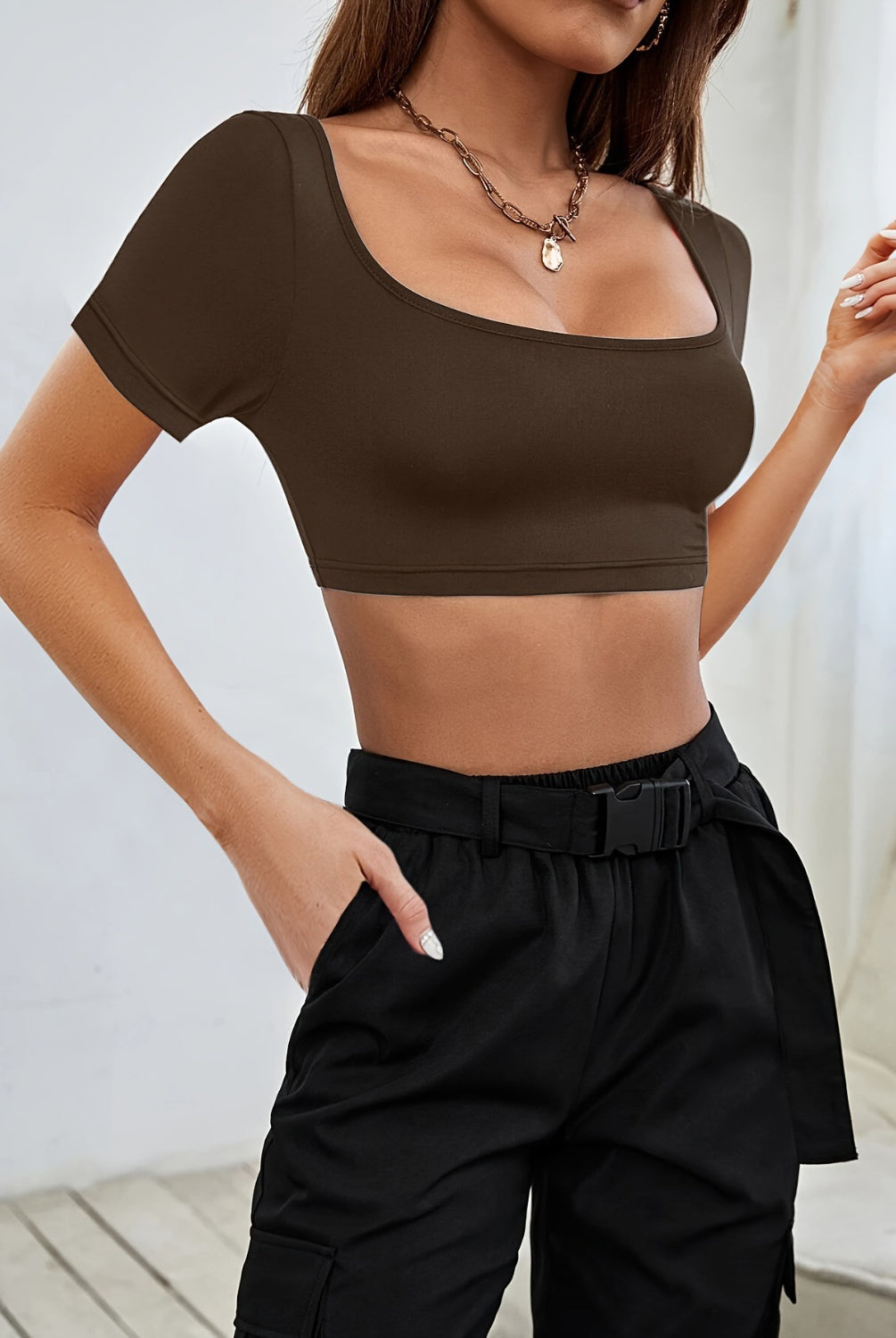 A stylish woman dons a sophisticated black crop top with a square neckline, paired seamlessly with high-waisted trousers for a sleek, urban look.