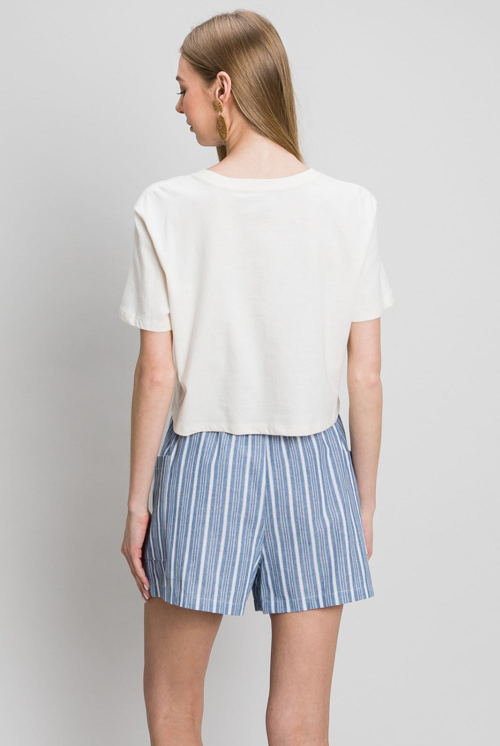 Woman wearing blue and white striped cotton shorts with a tie waist, paired with a white graphic t-shirt and gold hoop earrings.