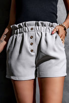 Fashion-forward woman sporting trendy grey paperbag waist shorts with a comfortable fit and button details.