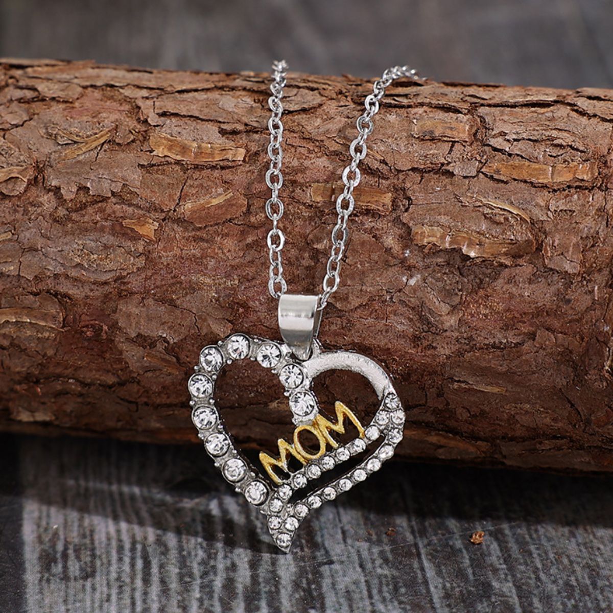 Charming 'Mom' heart pendant necklace with crystals on a rustic wooden backdrop.