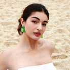 A woman by the beach embodies natural elegance with statement green leaf copper earrings, complementing her serene and graceful seaside style.