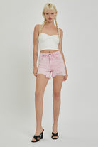 Model exuding summery charm in frayed pink denim shorts, perfect for a vibrant and playful daytime look.