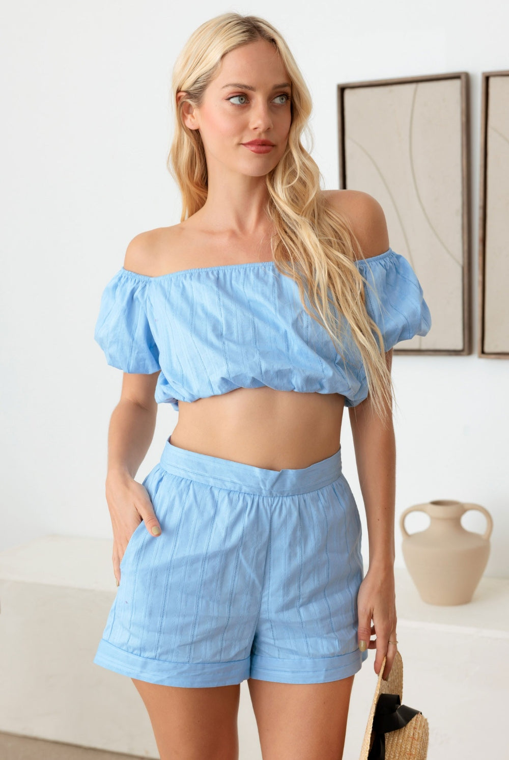 A woman wearing a sky blue off-shoulder crop top with matching shorts, creating a cohesive and stylish summer outfit.