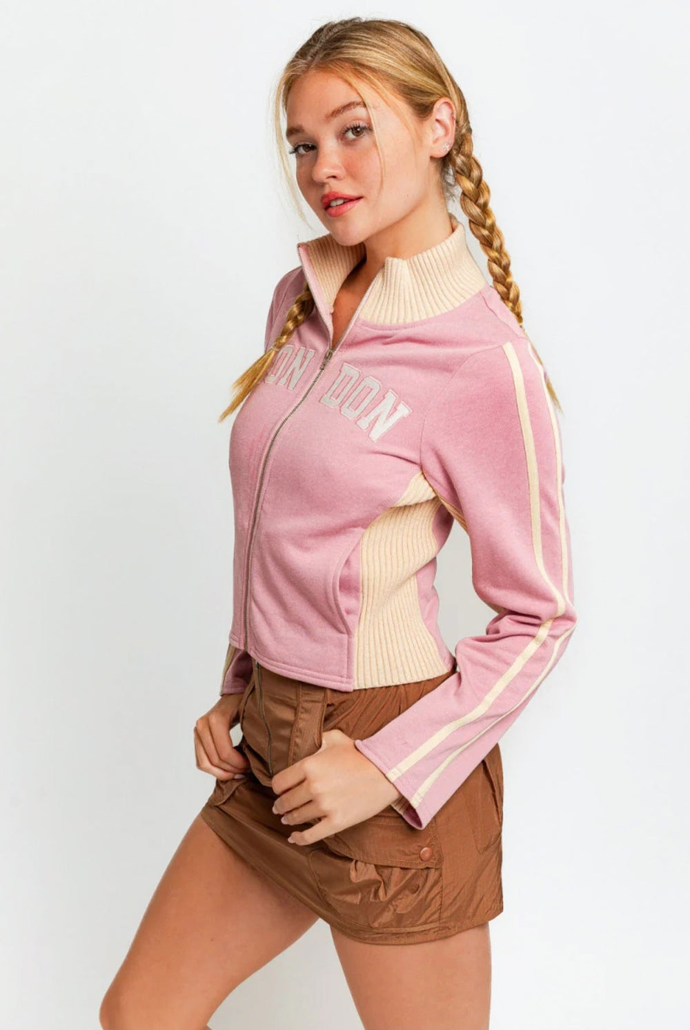 Trendy young woman showcasing a soft pink zip-up jacket with "LONDON" embroidered across the chest.