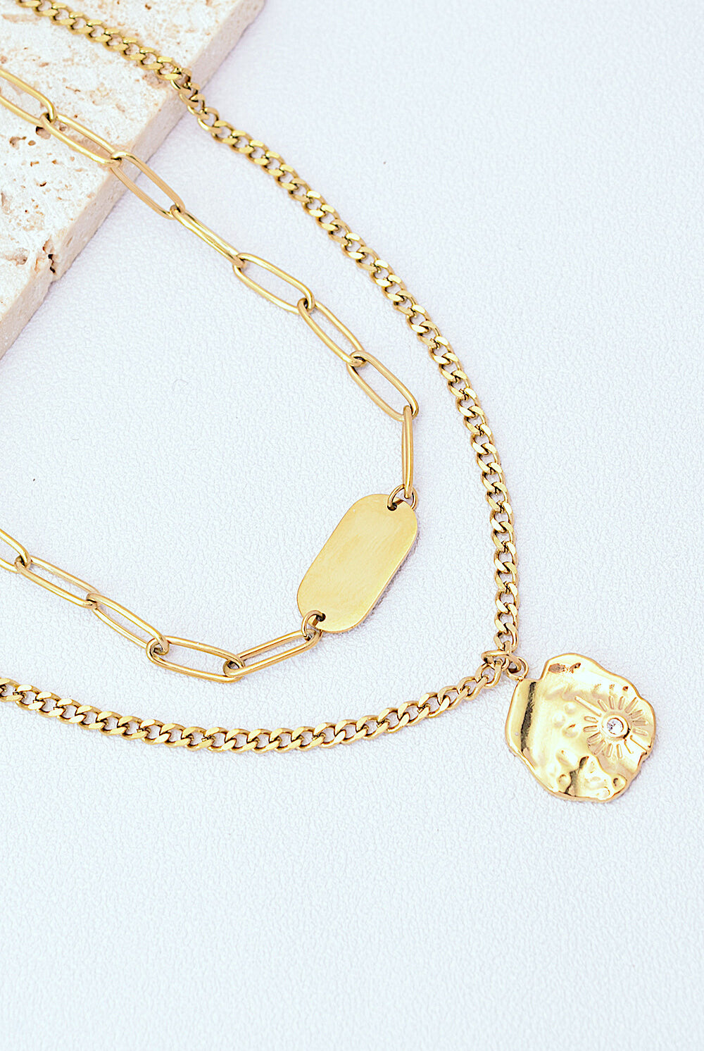 Gold-plated double-layered necklace featuring a bar detail on the upper chain and a detailed circular pendant on the lower chain, set against a white background.