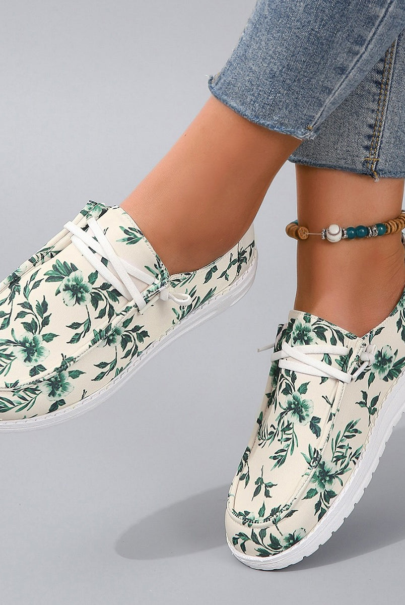 Woman's feet adorned with stylish lace-up sneakers featuring a botanical green leaf print on a light canvas.