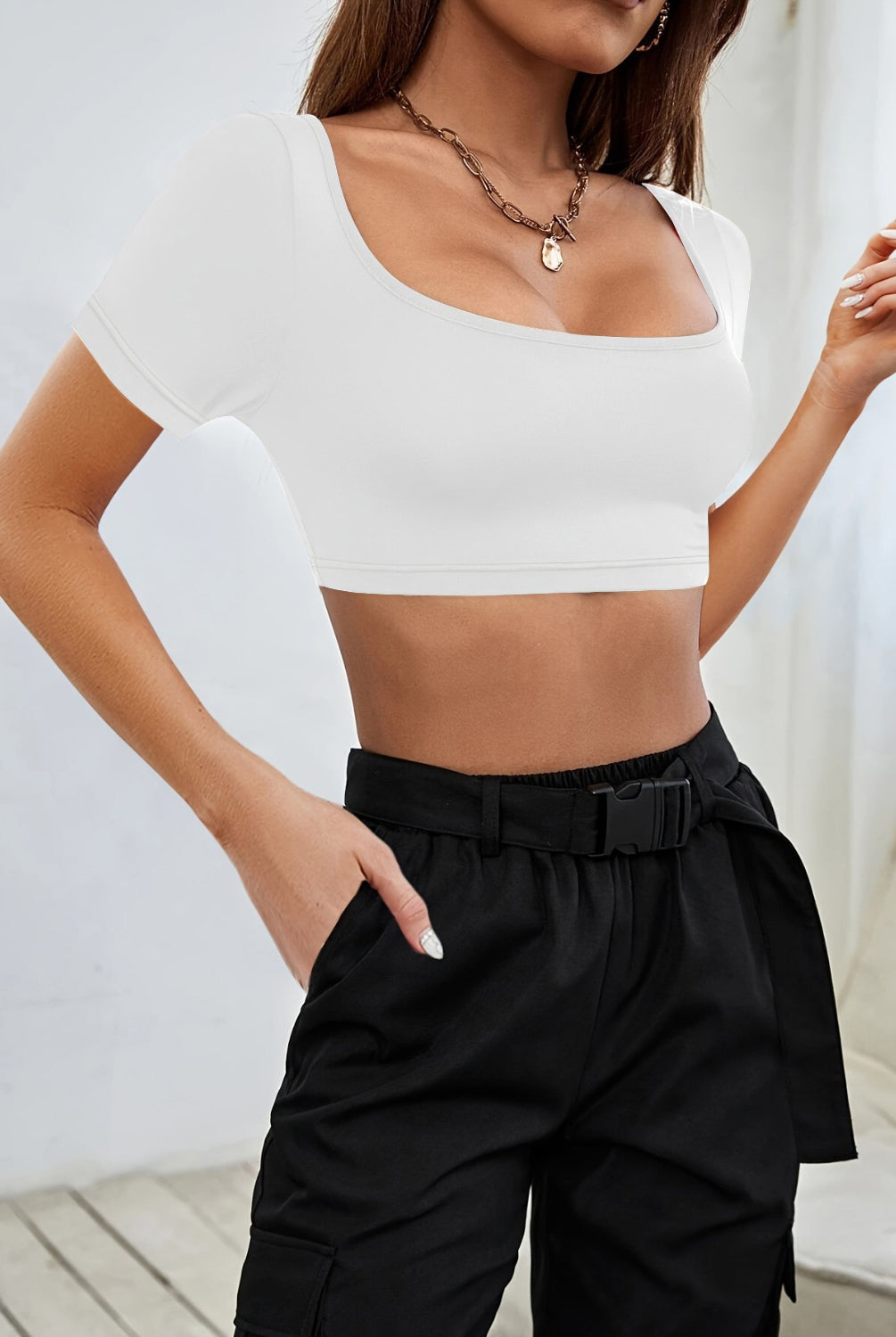 A stylish woman dons a sophisticated black crop top with a square neckline, paired seamlessly with high-waisted trousers for a sleek, urban look.