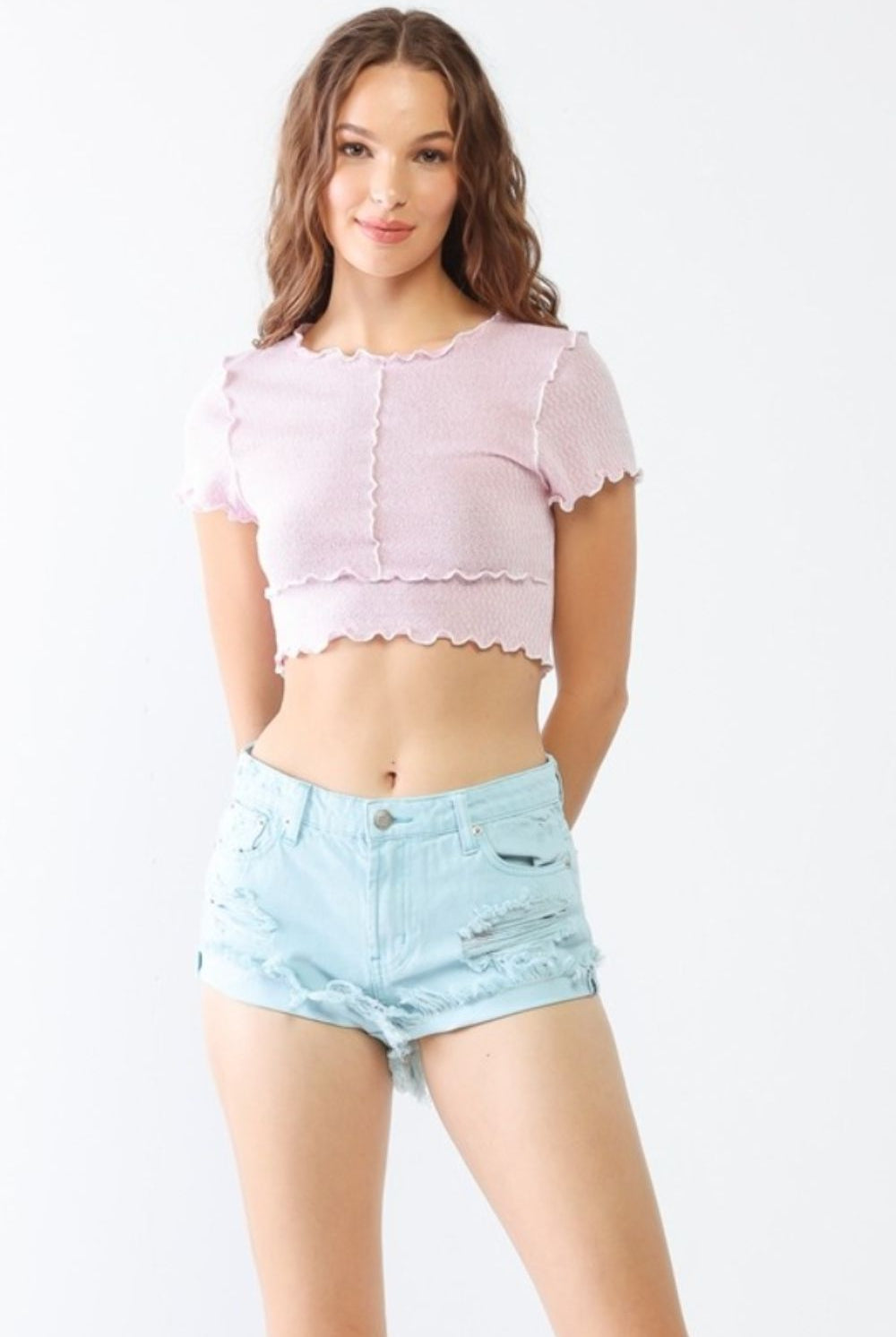 A model showcasing aqua ripped jean shorts with a distressed finish, paired with a soft pink cropped top for a summery, casual outfit.