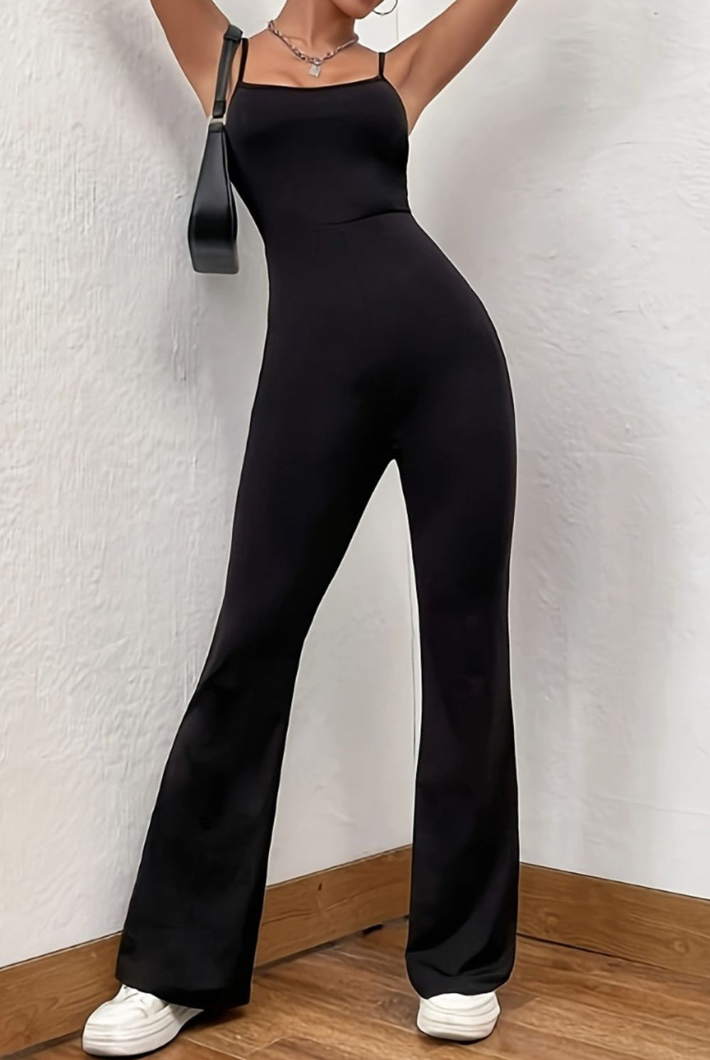 Chic and elegant woman in a sophisticated black spaghetti strap jumpsuit with a fitted bodice and flared legs, carrying a sleek bag, epitomizing modern style with a timeless appeal.