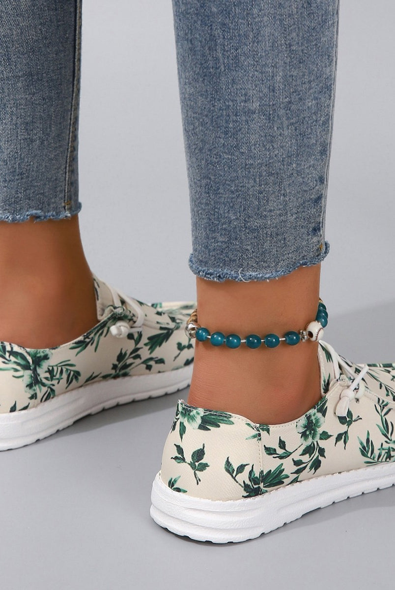 Woman's feet adorned with stylish lace-up sneakers featuring a botanical green leaf print on a light canvas.