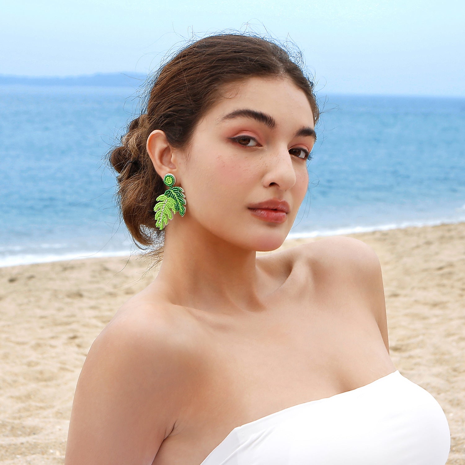 A woman by the beach embodies natural elegance with statement green leaf copper earrings, complementing her serene and graceful seaside style.