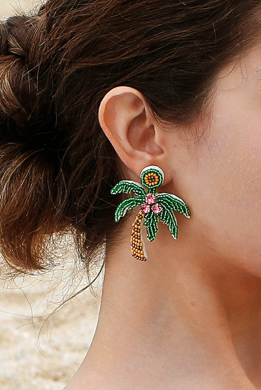 A woman exudes island grace with her stunning coconut tree beaded earrings, complementing her relaxed, seaside style with a touch of tropical elegance.