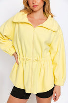 Chic young woman presenting a lemon yellow fleece jacket, ideal for adding a pop of color to a relaxed outfit.