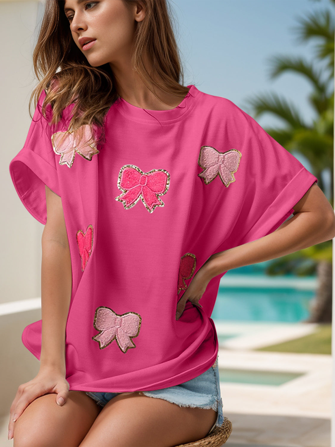 Three images of a woman wearing a sequin bow appliqué t-shirt, available in pink, white, and purple. Each shirt features decorative sequin bows, styled casually with denim shorts and worn by the model in a sunny, poolside setting.