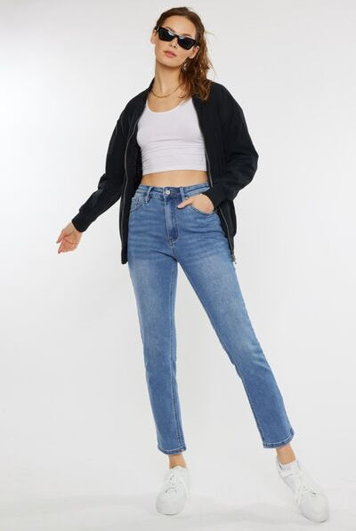 A model styled in casual attire, featuring cat whiskers high-waist jeans in light blue, complemented with a cropped white tank top, a black zip-up jacket, and white sneakers, exuding a relaxed and trendy vibe.