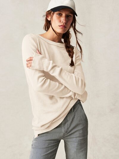 Model in a casual knit sweater with a ribbed texture and drop shoulders, paired with a baseball cap and jeans, embodying a relaxed and effortless style.