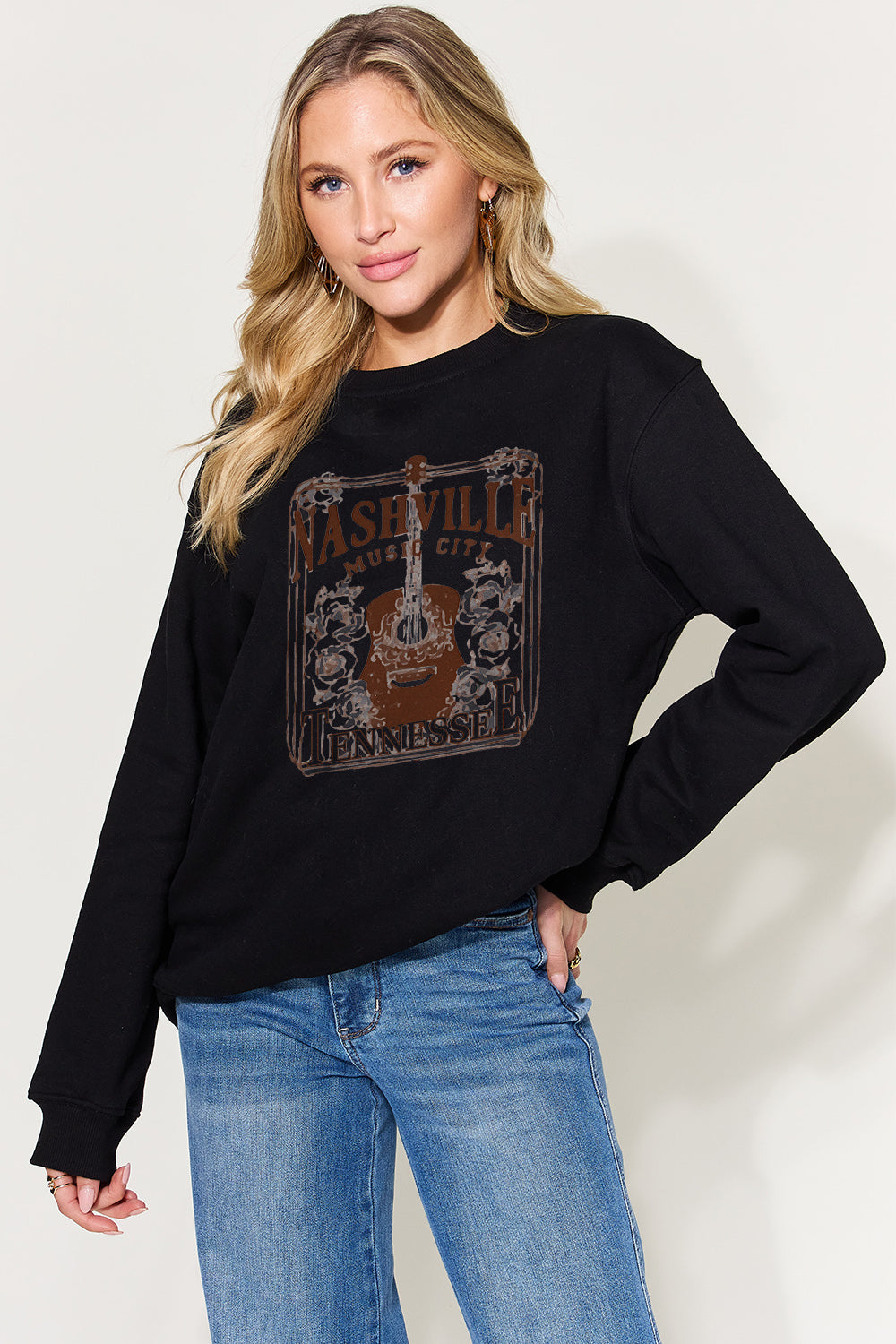 A woman models a heather gray 'Nashville Music City Tennessee' sweatshirt, displaying the vintage print design on the front, paired with blue jeans for a relaxed look.