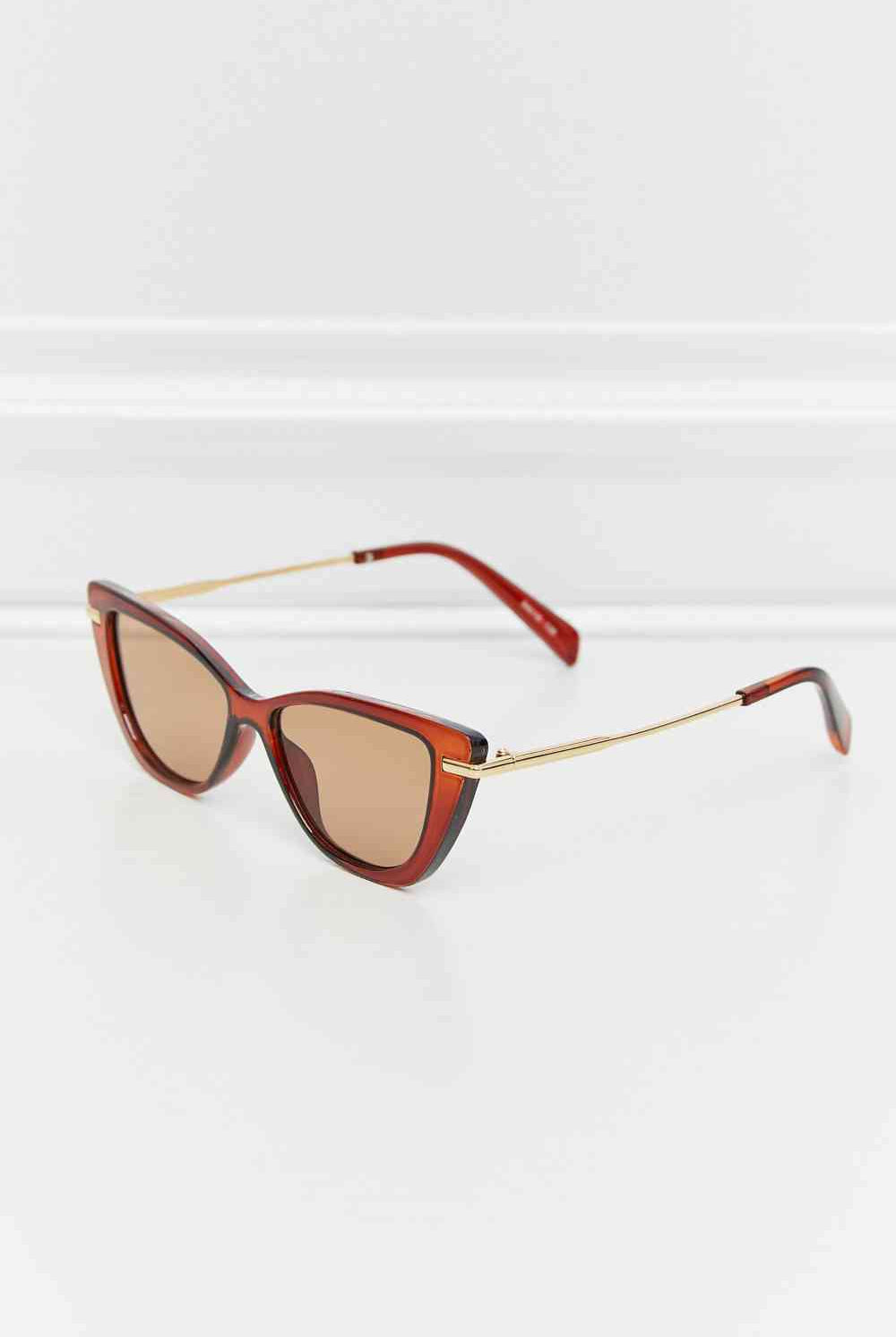 Woman wearing burgundy cat-eye sunglasses with a subtle gradient, paired with gold hoop earrings and a casual beige tank top, exuding a relaxed yet sophisticated summer vibe.
