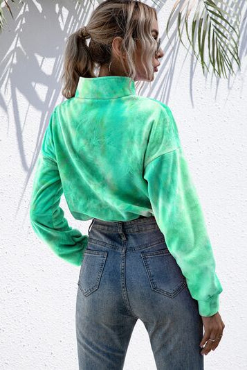 Woman in a tie-dye quarter-zip sweatshirt with drawstring hem, paired with distressed jeans and accessorized with round sunglasses, in a tropical setting with palm shadows.