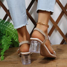 Elegant heeled sandals adorned with sparkling butterfly embellishments and a clear block heel, paired with chic ankle bracelets and frayed blue jeans.