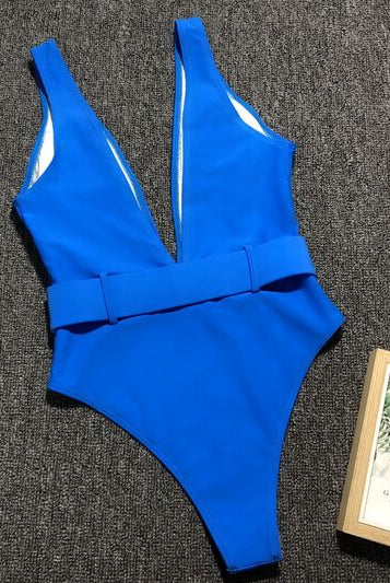 Model showcasing a vibrant blue sleeveless one-piece swimsuit with a deep V-neckline and a belted waist, perfect for a stylish beach day.