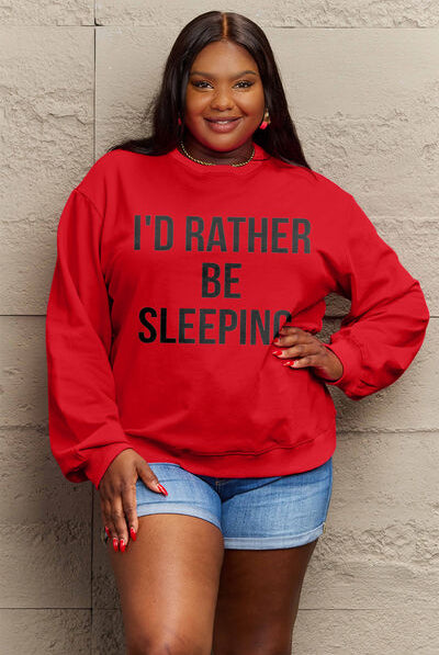 Woman modeling a red round neck sweatshirt with the text "I'D RATHER BE SLEEPING" printed on the front, paired with white shorts.
