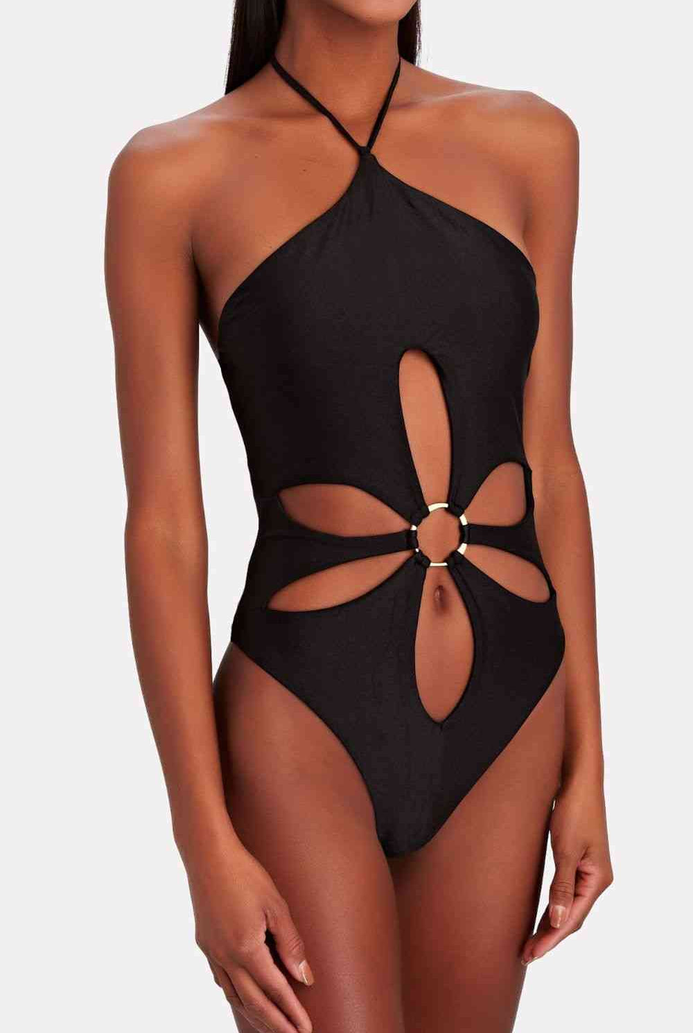  Olive green, halter neck one-piece swimsuit with floral cut-out details around the waist and chest, worn by a model posing in a tropical jungle setting.