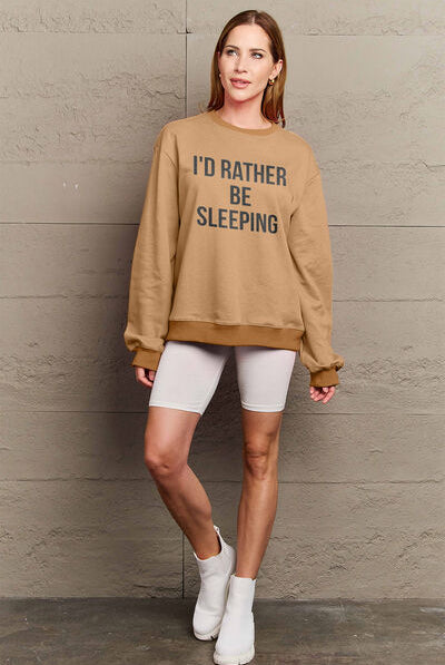 Woman modeling a brown round neck sweatshirt with the text "I'D RATHER BE SLEEPING" printed on the front, paired with white shorts.