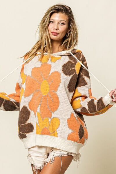 A woman wearing an oversized knit hoodie sweater with a bold floral pattern, casual for a relaxed and stylish look.