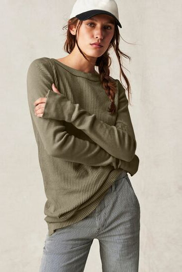 Model in a casual knit sweater with a ribbed texture and drop shoulders, paired with a baseball cap and jeans, embodying a relaxed and effortless style.