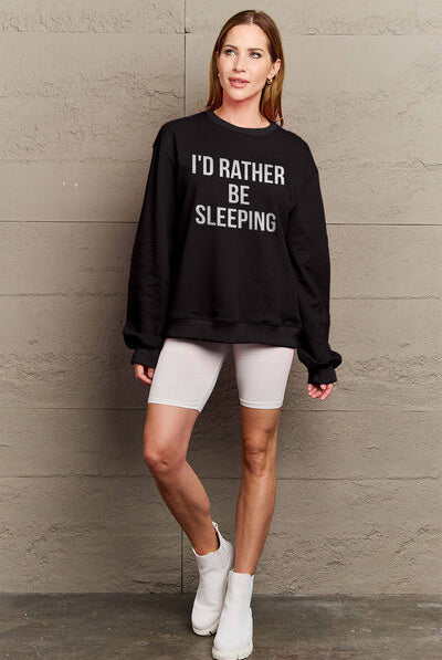 Woman modeling a black round neck sweatshirt with the text "I'D RATHER BE SLEEPING" printed on the front, paired with white shorts.