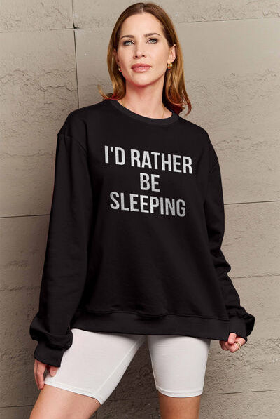 Woman modeling a black round neck sweatshirt with the text "I'D RATHER BE SLEEPING" printed on the front, paired with white shorts.
