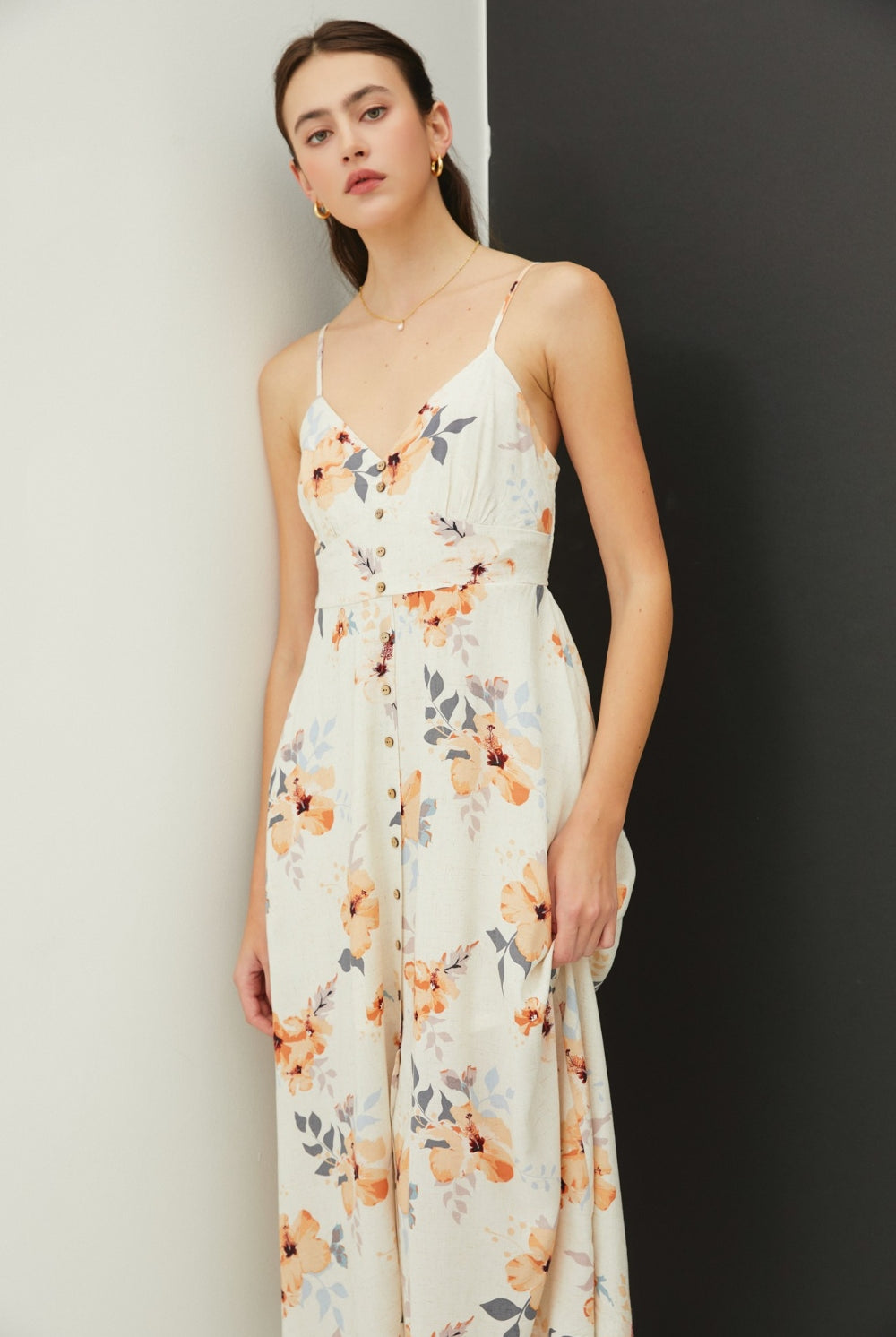 A model is gracefully poised in a botanical print midi dress with a button-front detail, adjustable straps, and a flared skirt, exemplifying casual elegance.