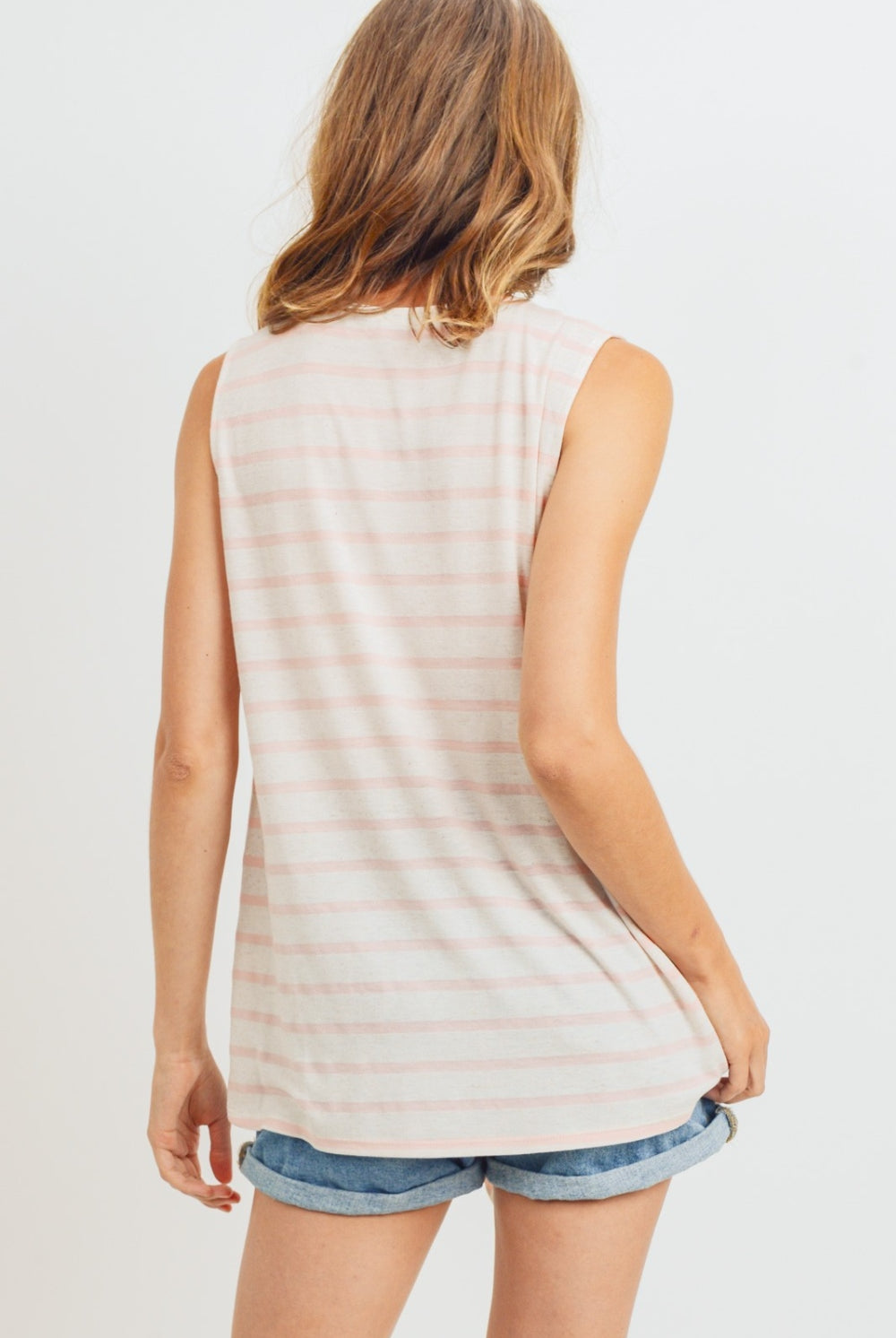 A woman in a coral and white striped sleeveless cotton top with a front tie detail, pairing it casually with denim shorts for a relaxed and stylish summer look.