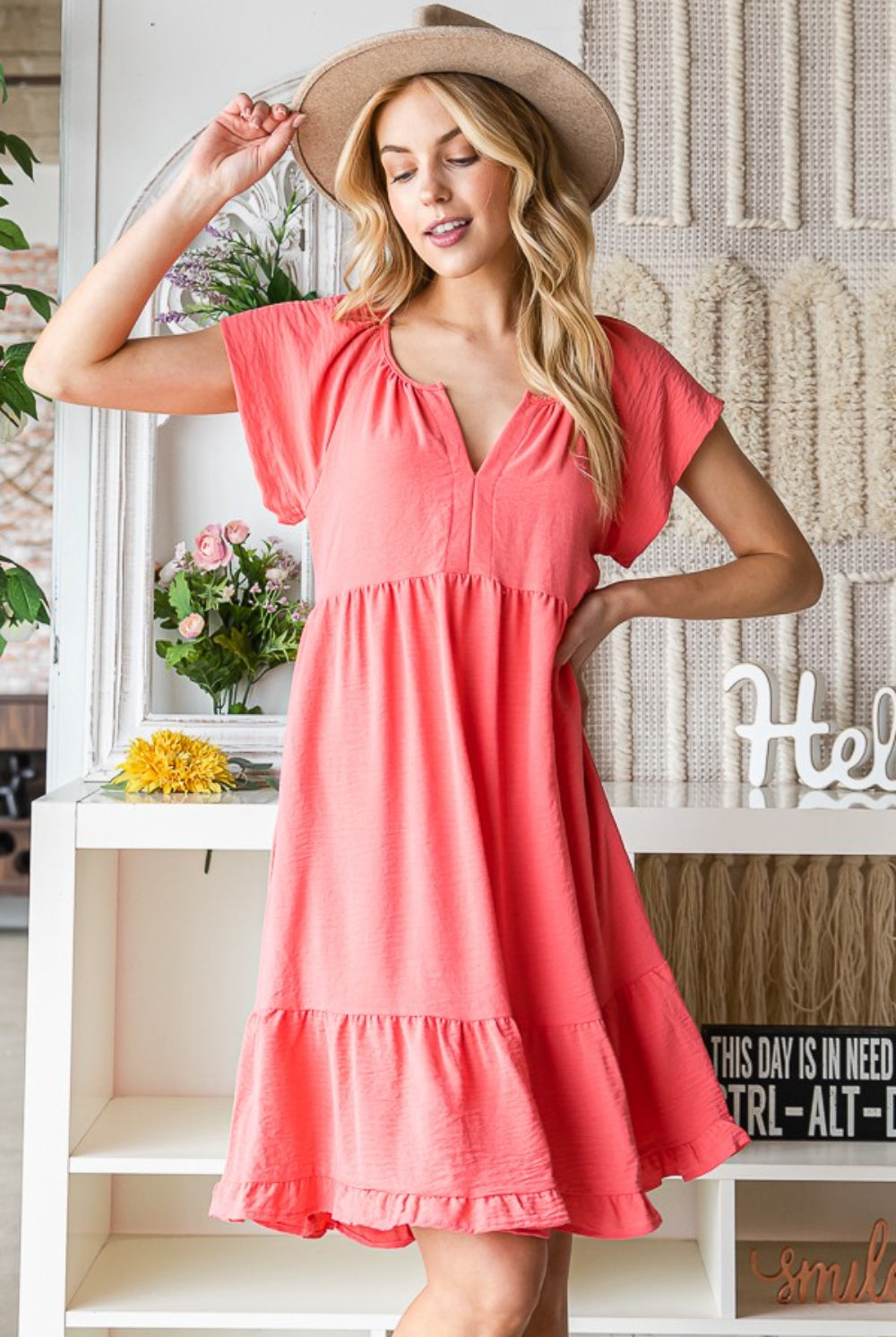 Woman smiling in a radiant coral summer dress with cap sleeves and ruffled hem.