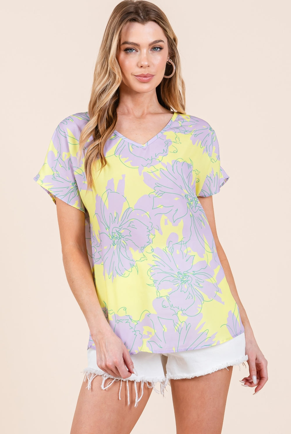 A woman wearing a vibrant yellow and purple floral short sleeve t-shirt, styled casually with white distressed shorts for a fresh, summery look.