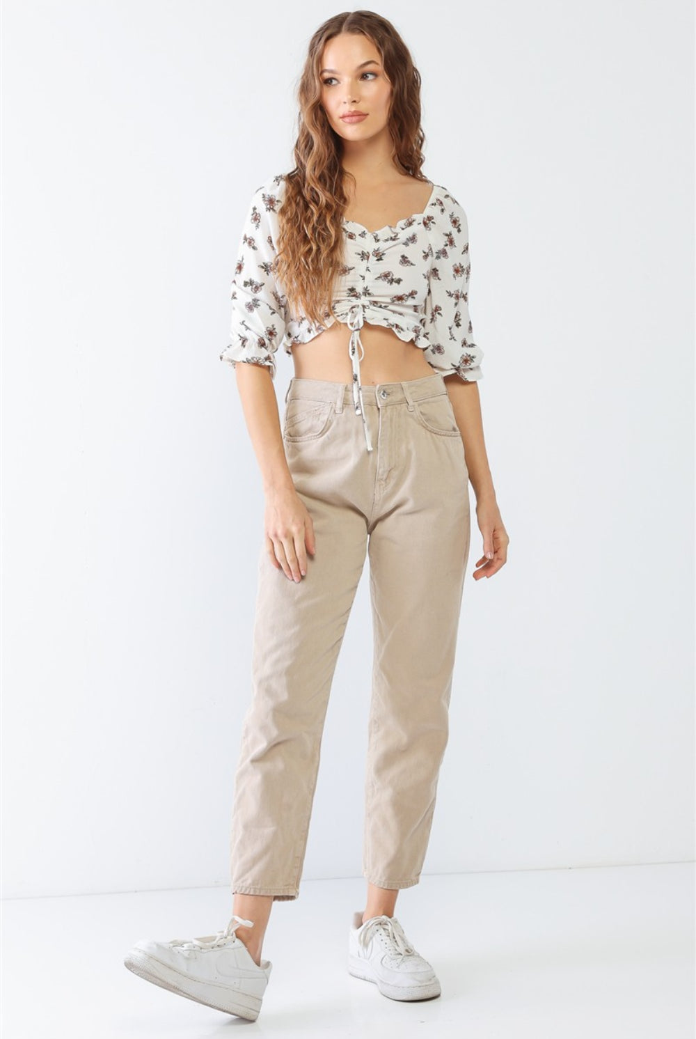 A woman in a white floral ruffled crop top, paired with casual beige pants for a fresh and trendy look.