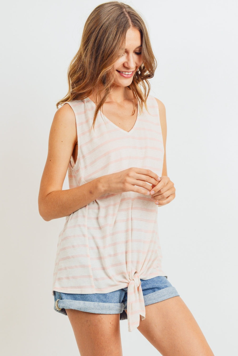 A woman in a coral and white striped sleeveless cotton top with a front tie detail, pairing it casually with denim shorts for a relaxed and stylish summer look.