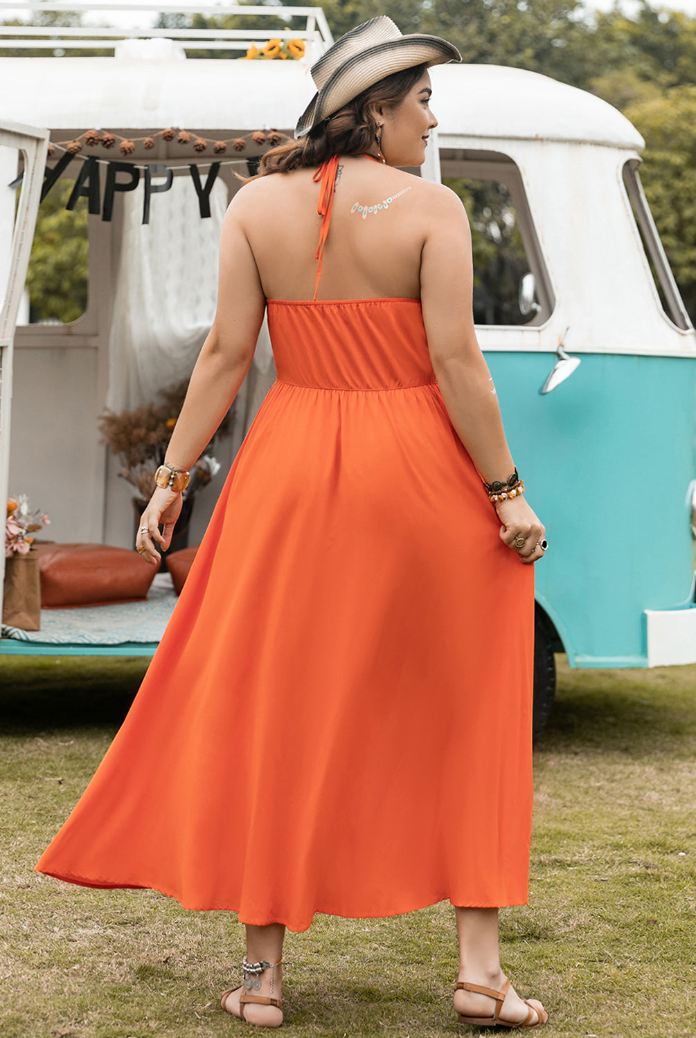 Woman wearing a vibrant orange plus size halter neck midi dress, standing in front of a decorated camper van.