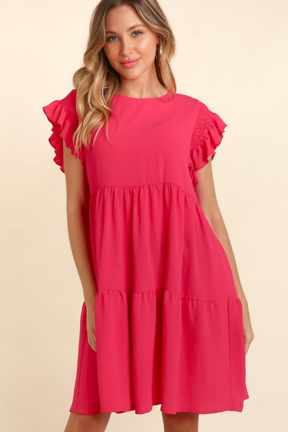 Woman wearing a fuchsia short sleeve ruffle dress with pockets, smiling and posing with arms crossed.