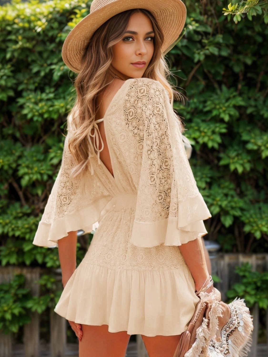 Fashionable woman posing in a cream lace-back mini dress with ruffle details