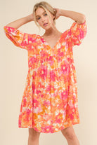 Woman wearing a vibrant floral print long sleeve dress in shades of orange and pink, featuring a tie back detail.