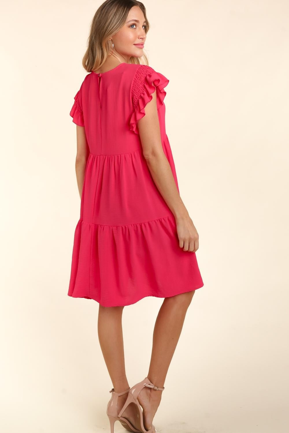 Woman wearing a fuchsia short sleeve ruffle dress with pockets, smiling and posing with arms crossed.