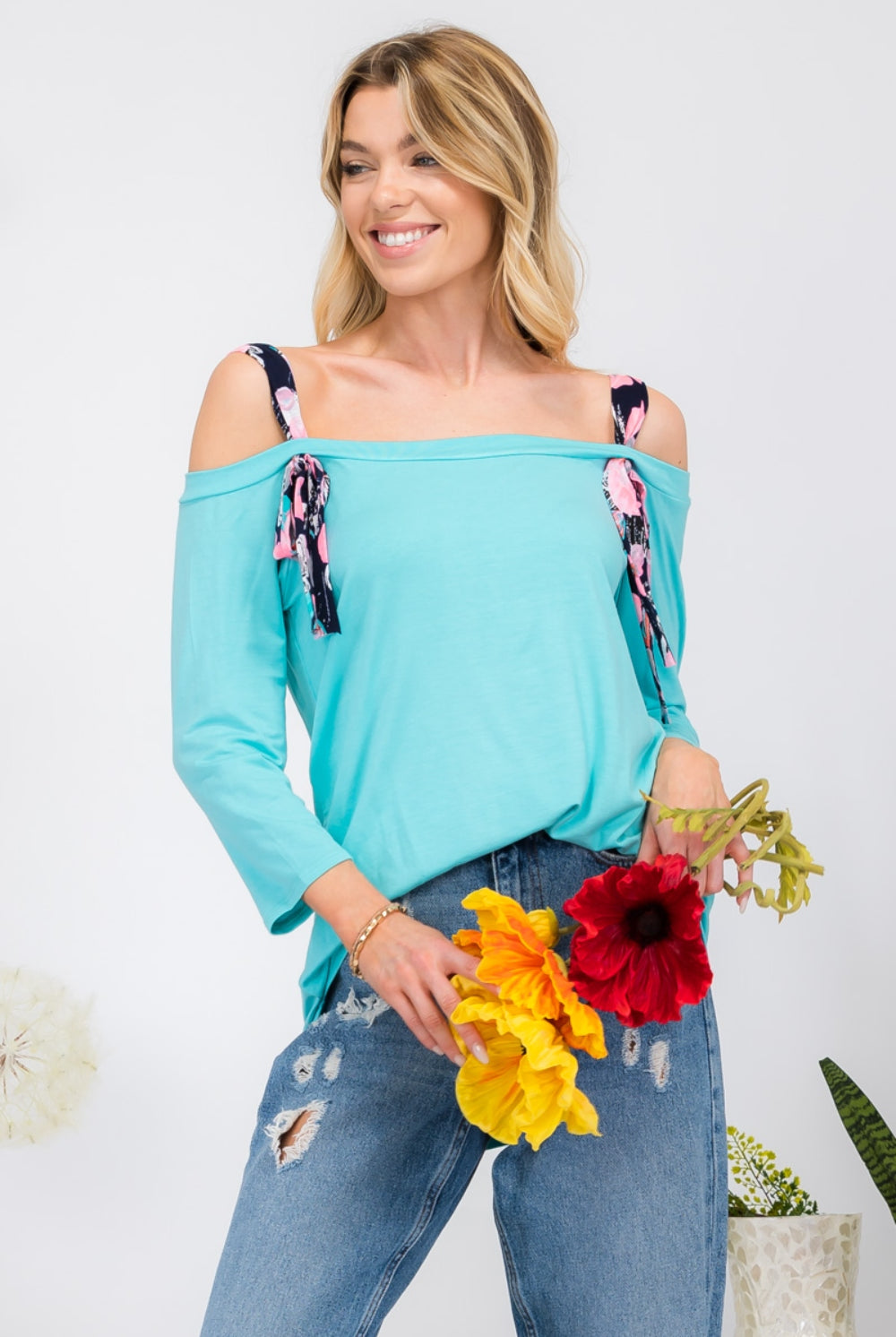 Smiling woman wearing a Sky Blue Off-Shoulder Blouse with floral tie sleeves, creating a playful yet elegant look, available at GemThreads Boutique.