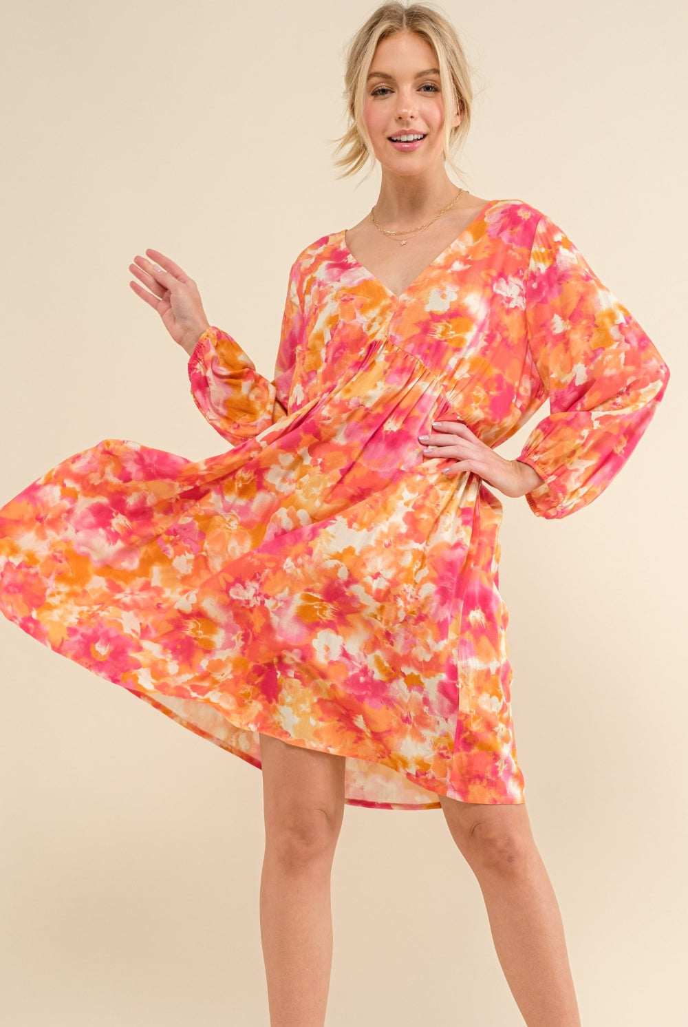 Woman wearing a vibrant floral print long sleeve dress in shades of orange and pink, featuring a tie back detail.